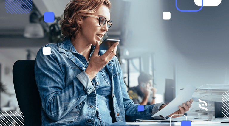 mulher loira de óculos de grau sentada e com smartphone próximo a boca utilizando o voice banking